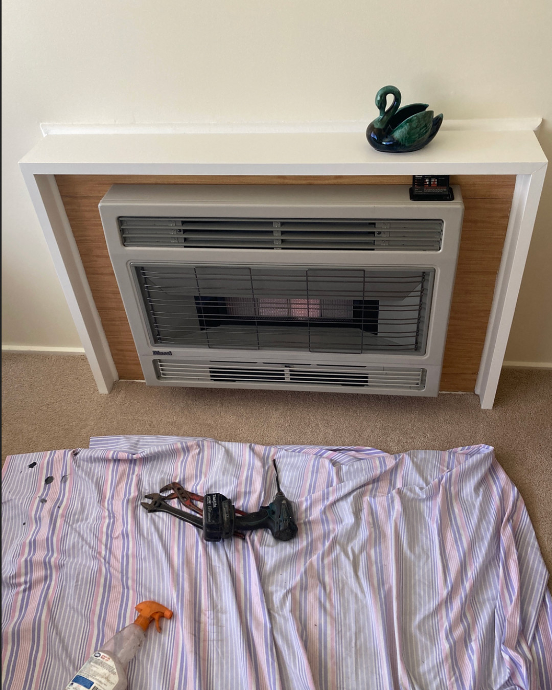 A gas space heater being serviced in a customer's lounge room, drop sheet down and tools laid out
